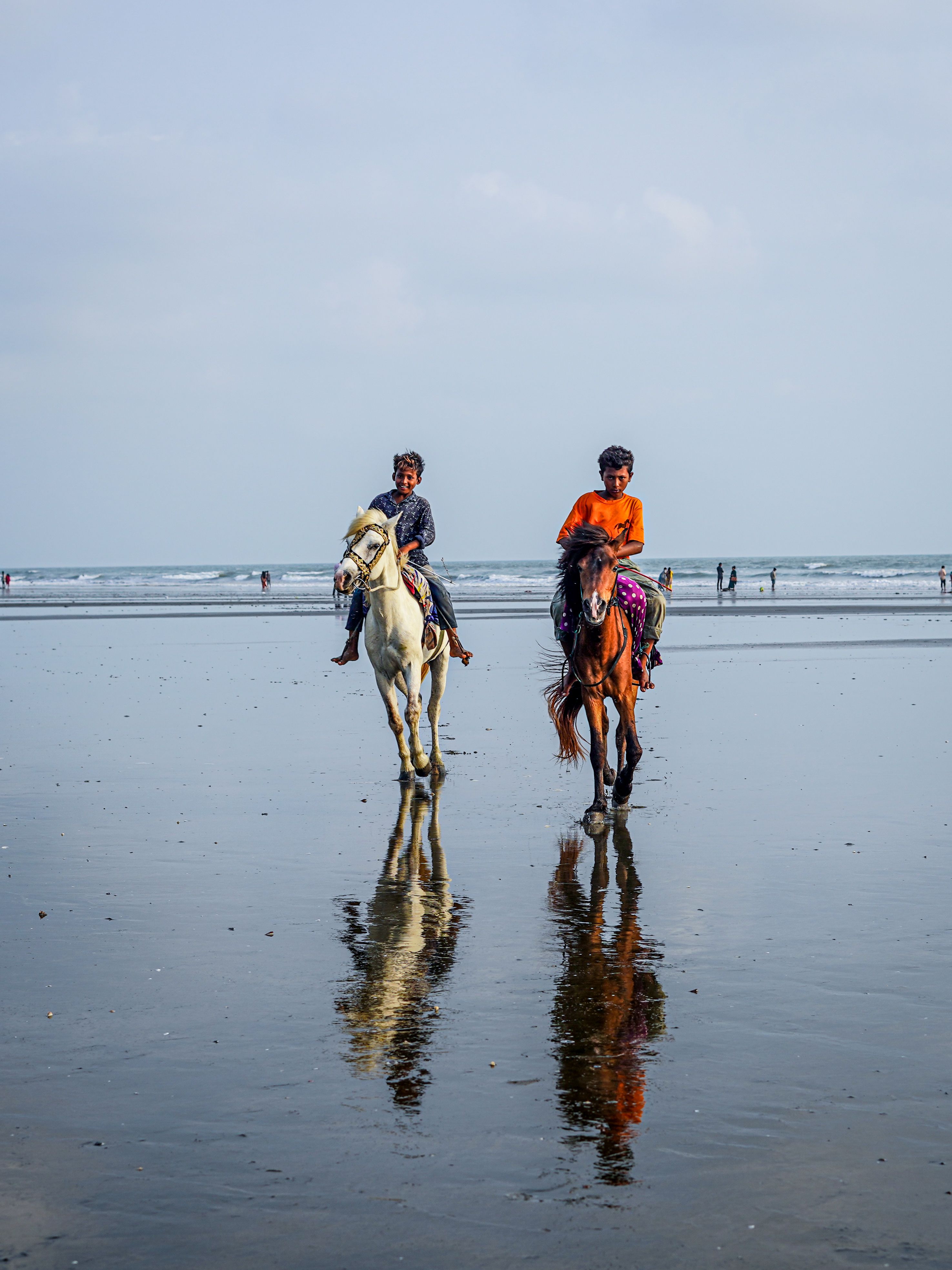 Two men horseback riding on a sandy beach