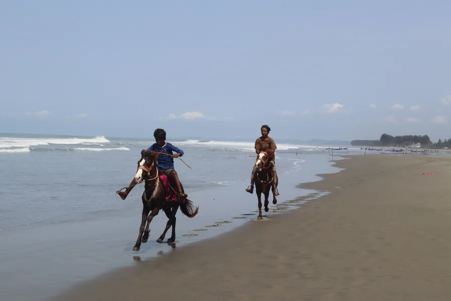 Two people enjoy horseback riding along a serene beach